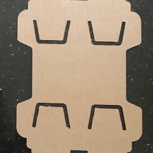 May include: A brown cardboard template with four cut-out shapes for holding cups or glasses. The template is designed to be folded and assembled into a holder for multiple cups.