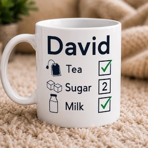 May include: A white ceramic mug featuring the name David in dark blue text. Below the name is a checklist with icons for tea, sugar, and milk. The tea and milk lines have green checkmarks, while the sugar line contains the number 2 in a box.