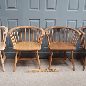 Op de afbeelding: Vier houten stoelen met een gebogen rugleuning en een spindelontwerp. De stoelen zijn in verschillende stadia van vlekken, van licht tot donker. De stoelen zijn in een rij op een houten vloer voor een grijze muur geplaatst. De tekst "CHAIR-SUPPLY" is zichtbaar op een houten bord voor de stoelen.