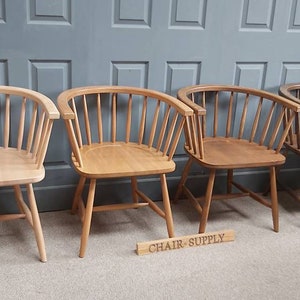 Op de afbeelding: Vier houten stoelen met een gebogen rugleuning en een spindelrug. De stoelen zijn in verschillende houttinten, van licht tot donker. De stoelen zijn in een rij op een tapijt gelegd. Een bord met de tekst "CHAIR-SUPPLY" staat op de voorgrond.