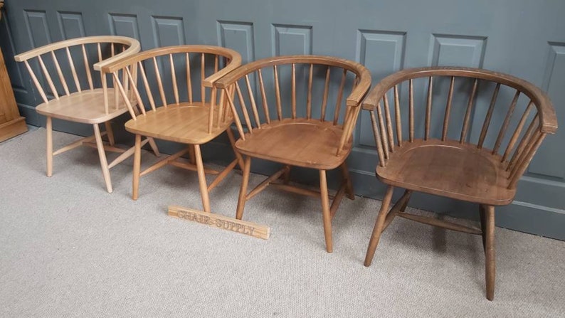 Op de afbeelding: Vier houten stoelen met een gebogen rugleuning en een latten ontwerp. De stoelen zijn in verschillende tinten bruin, van licht tot donker.