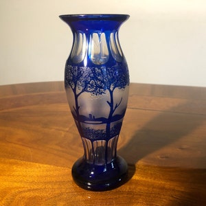 May include: A cobalt blue glass vase with a frosted design of trees and a landscape. The vase has a flared top and a round base.