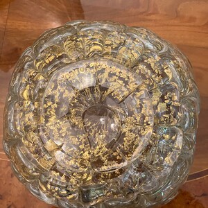May include: A clear glass bowl with a textured surface and gold flecks throughout. The bowl is round and has a wide opening.