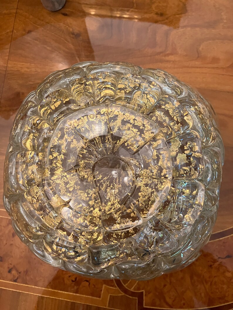 May include: A clear glass bowl with a textured surface and gold flecks throughout. The bowl is round and has a wide opening.