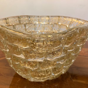 May include: A clear glass bowl with a textured, woven design and gold flecks throughout. The bowl has a wide, rounded base and a slightly flared rim.