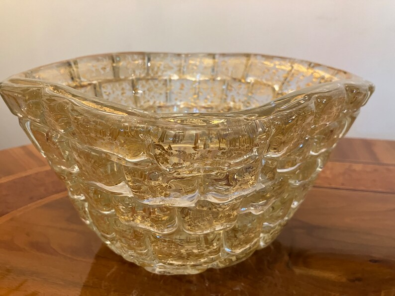 May include: A clear glass bowl with a textured, woven design and gold flecks throughout. The bowl has a wide, rounded base and a slightly flared rim.