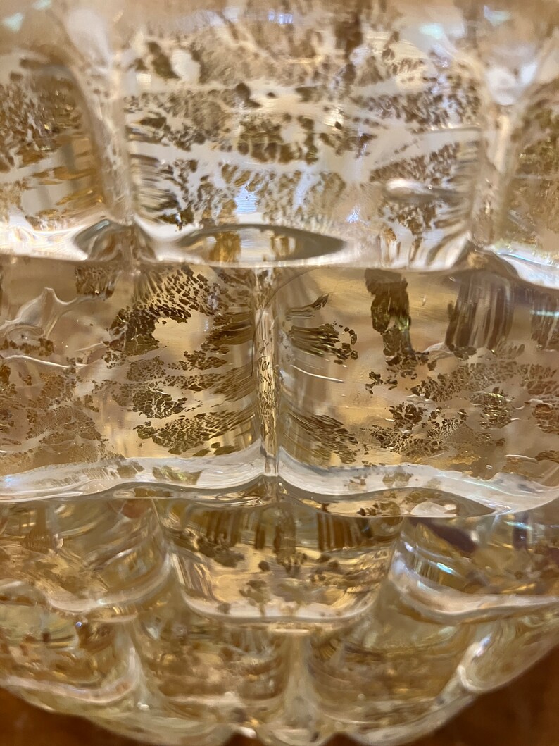 May include: A clear glass vase with a textured surface and gold flecks throughout. The vase has a rounded shape with a wide opening at the top.