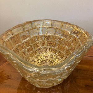 May include: A clear glass bowl with a textured surface and gold flecks throughout. The bowl has a square shape with rounded edges.