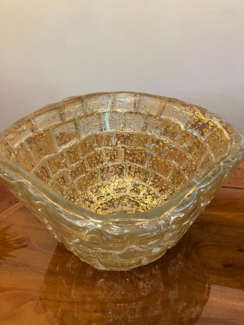 May include: A clear glass bowl with a textured surface and gold flecks throughout. The bowl has a square shape with rounded edges.