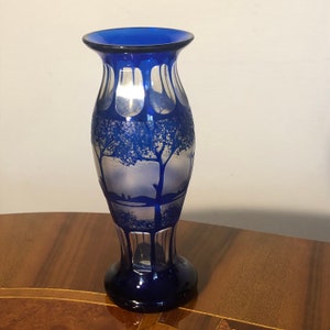 May include: A cobalt blue glass vase with a frosted design of trees and a landscape. The vase has a rounded body and a flared lip.
