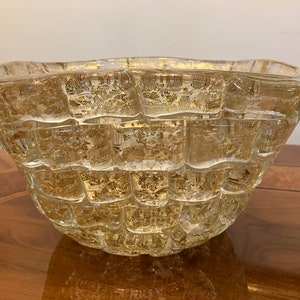 May include: A clear glass bowl with a textured, woven design. The bowl has a gold-like sheen and is perfect for serving snacks or holding decorative items.