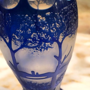 May include: A blue glass vase with a frosted design of trees. The vase has a textured surface and a rounded bottom.
