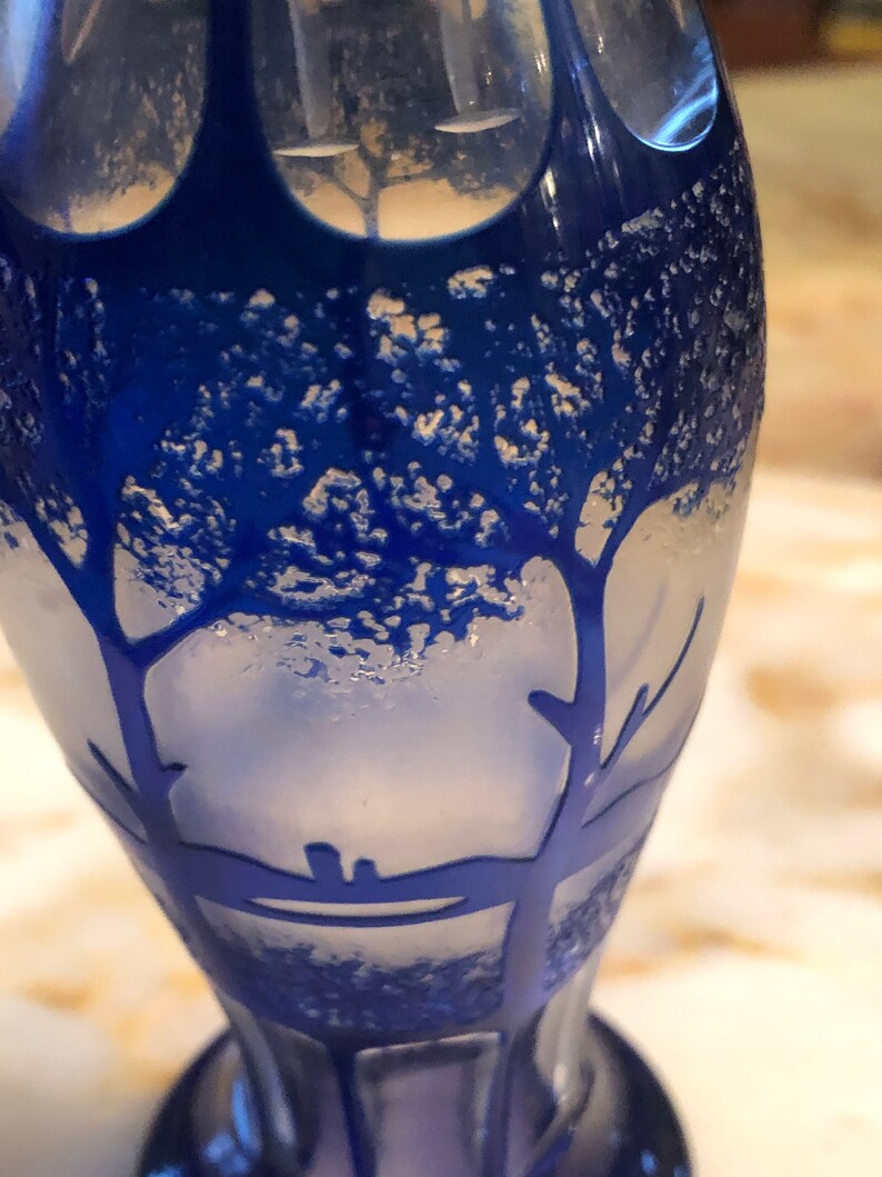 May include: A blue glass vase with a frosted design of trees. The vase has a textured surface and a rounded bottom.