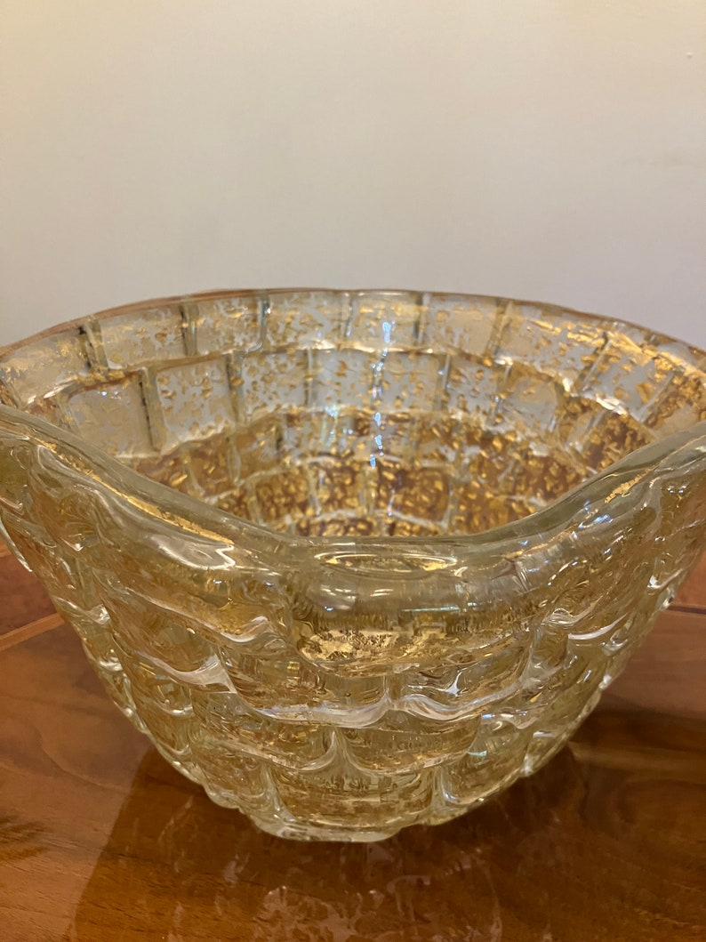 May include: A clear glass bowl with a textured, woven design and gold flecks throughout. The bowl has a rounded shape and a wide rim.