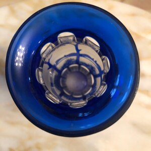 May include: A blue glass bottle stopper with a clear, decorative top featuring a geometric design.
