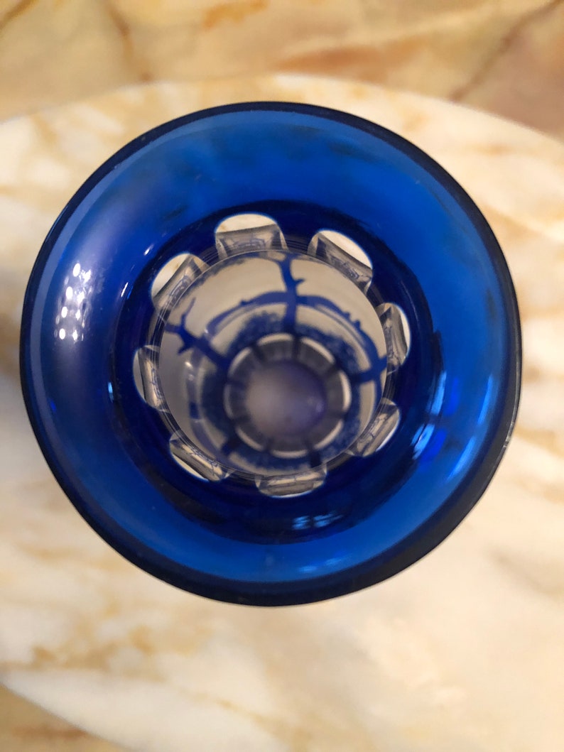 May include: A blue glass bottle stopper with a clear, decorative top featuring a geometric design.