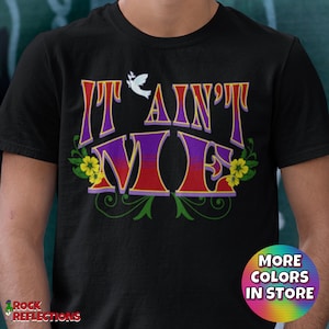 May include: Black t-shirt with the text "It Ain't Me" in a colorful, retro font with a white dove and yellow flowers.