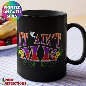 May include: Black coffee mug with a white dove and the text "It Ain't Me" in colorful letters with floral accents.