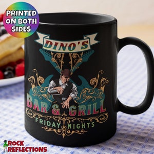 May include: Black ceramic mug with a colorful graphic design featuring a cartoon character playing a guitar. The text on the mug reads "Dino's Bar & Grill Friday Nights".
