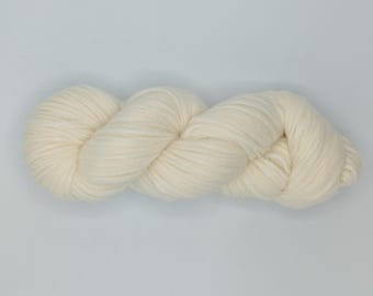 May include: A skein of ivory-colored yarn, tightly twisted and coiled, lies against a plain white background. The yarn appears soft and thick, suitable for knitting or crocheting projects. The texture is visible, suggesting a natural fiber.