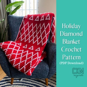 Op de afbeelding: Een rood-witte gehaakte deken met een ruit- en driehoekpatroon, gedrapeerd over een blauwe fauteuil. De deken heeft een textuurontwerp met witte bobbles. De tekst luidt "Holiday Diamond Blanket Crochet Pattern (PDF Download)".