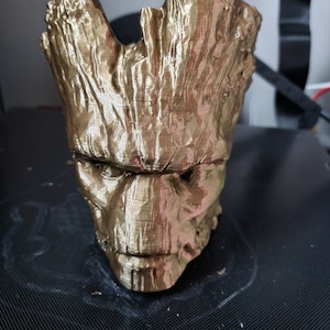 May include: A gold-coloured 3D printed planter shaped like the head of the character Groot from the Guardians of the Galaxy movie franchise.