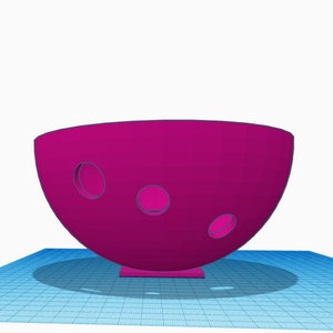 May include: A magenta-colored ceramic bowl with three circular cutouts. The bowl has a rounded bottom and a flat base.
