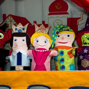 Puede incluir: Cinco marionetas de fieltro de colores en un escenario. Las marionetas incluyen un diablo rojo, un príncipe azul y blanco, una princesa rosa, un bufón verde y amarillo y una bruja morada y verde.