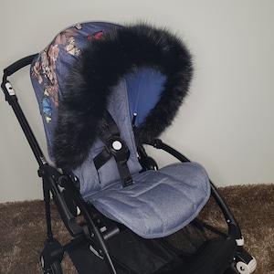 Könnte beinhalten: Ein schwarzer Kunstfell-Kinderwagen-Einsatz mit einem blauen Jeans-Kinderwagen-Sitz und einem Baldachin mit Schmetterlingsmuster.