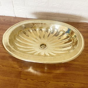 May include: A gold oval-shaped bathroom sink with a decorative, fluted design. The sink has a single drain hole in the center.