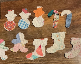 May include: A collection of ten quilted fabric ornaments in various shapes including snowmen, candy canes, gingerbread people, and stockings. Each piece features a unique patchwork design with assorted floral, plaid, and solid coloured cotton fabrics.