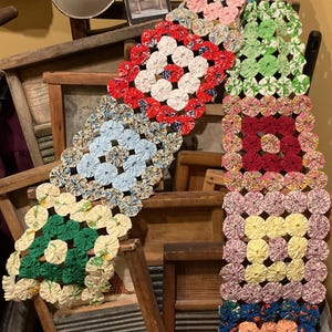 May include: A collection of colorful, handmade fabric items, including a long, multi-colored runner and several square pieces. The runner features a variety of colors, including red, blue, green, and pink, and is made of small, circular fabric pieces.