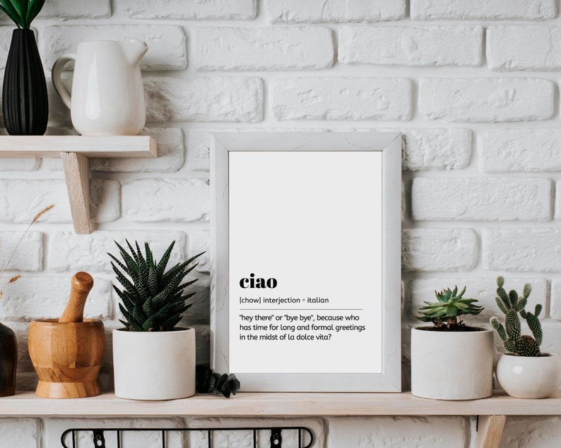 May include: A white framed print with the word "ciao" in bold black text. The definition of the word is written in smaller black text below. The definition reads: "[chow] interjection - Italian "hey there" or "bye bye", because who has time for long and formal greetings in the midst of la dolce vita?"