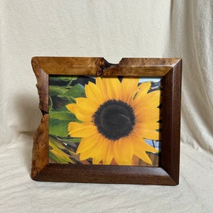 May include: A wooden picture frame with a natural wood finish and a sunflower image inside. The frame has a unique, irregular shape and a dark brown stain.