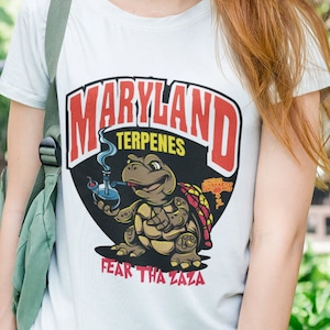 May include: White t-shirt with a red, black, and yellow graphic of a turtle smoking a bong. The graphic includes the text "Maryland Terpenes" and "Fear Tha Zaza".