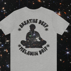 May include: A gray t-shirt with a black graphic design featuring a silhouette of a person meditating with the text "Breathe Deep *Melanin Drip*" in a dripping font.