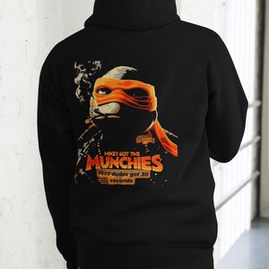 May include: Black hooded sweatshirt featuring a graphic of a Teenage Mutant Ninja Turtle smoking a cigarette and holding a pizza box. The graphic reads "Mikey got the munchies" and "Pizza dudes got 30 seconds".
