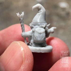 Pu&ograve; includere: Una miniatura di gnomo in plastica grigia stampata in 3D che indossa un cappello a punta e porta un bastone. Lo gnomo indossa uno zaino e ha un'espressione amichevole. La miniatura &egrave; in piedi su una base rotonda.