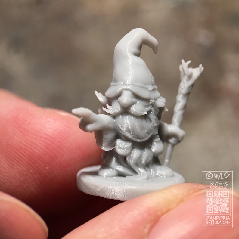 Pu&ograve; includere: Una miniatura grigia di un mago stampata in 3D con un cappello a punta, barba e bastone. La miniatura &egrave; in piedi su una base rotonda. Il testo "OWS 2023" e un codice QR sono visibili sullo sfondo.