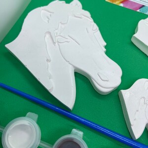 May include: A paint-your-own horse head figurine with a white paint finish. The figurine is part of a craft kit that includes paint pots and a paintbrush.
