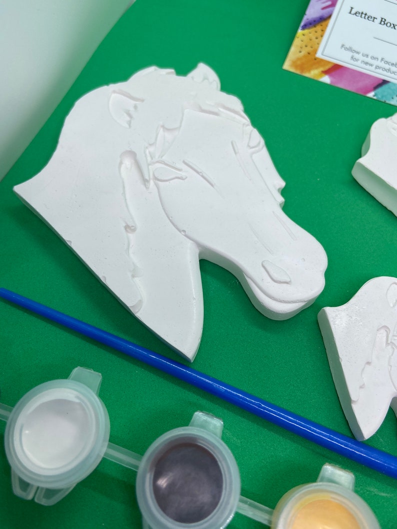 May include: A paint-your-own horse head figurine with a white paint finish. The figurine is part of a craft kit that includes paint pots and a paintbrush.