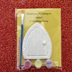 May include: A craft kit for a 5th birthday party. It includes a white ceramic door, three small paint pots, a paintbrush, and a card that says "Thank you for coming to Louise's 5th Birthday Party".