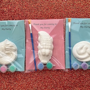 May include: Three paint-your-own party favours, each in a clear plastic bag. The favours include a small ceramic figurine, a paintbrush, and a small container of paint. The figurines are a chameleon, a corn cob, and a snake. The bags have a blue background with the text "Thank you for coming to My Party".