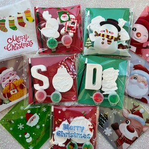 May include: A selection of Christmas craft kits, each containing a paintable ceramic figure, paint pots, and a brush. Designs include a snowman, Santa, reindeer, and baubles. Some kits feature the words "Merry Christmas".