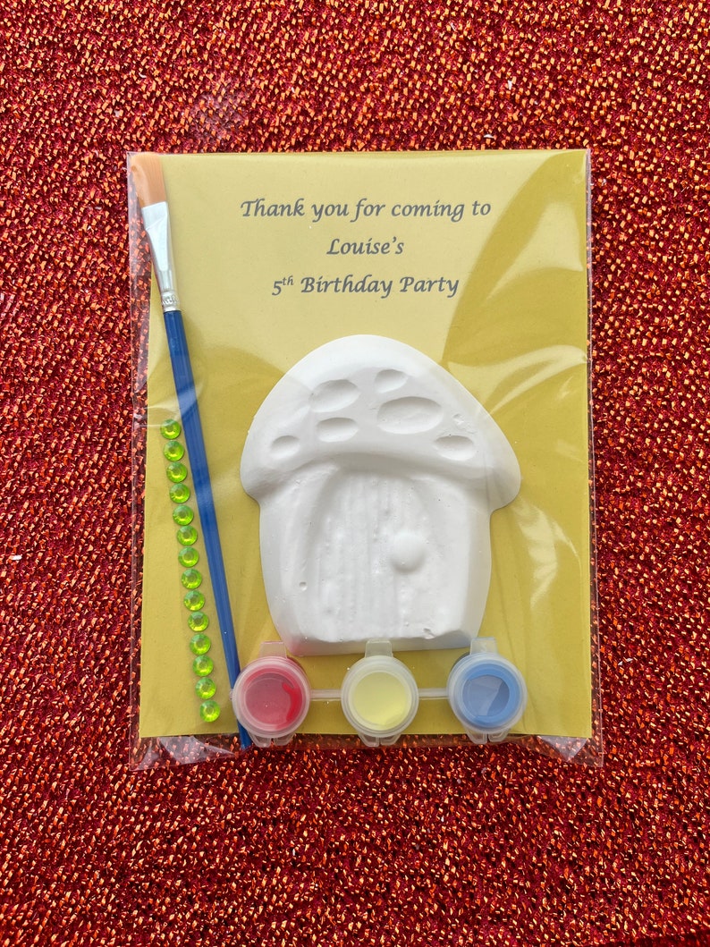 May include: A yellow and white paint-your-own mushroom house craft kit. The kit includes a white ceramic mushroom house, three small paint pots, a paintbrush, and green rhinestones. The card reads "Thank you for coming to Louise's 5th Birthday Party."