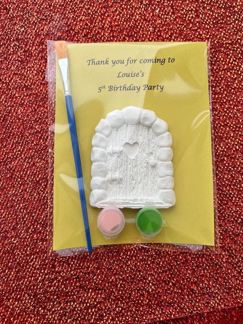 May include: A craft kit for a 5th birthday party. It includes a white plaster fairy door, a paintbrush, pink and green paint, and a thank you note that says "Thank you for coming to Louise's 5th Birthday Party".