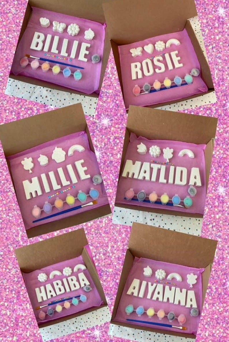May include: Five pink boxes with white letters spelling out names, each box contains paint pots and a paintbrush. The names are Billie, Rosie, Millie, Matilda, and Habiba.