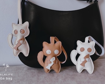May include: Three leather cat keychains with a fish design. The keychains are hanging on a black leather bag. The text "LALALIFE On bag" is visible at the bottom of the image.