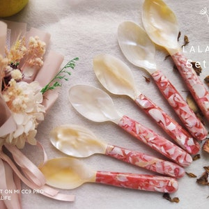 Könnte beinhalten: Sechser-Set aus Perlmuttlöffeln mit pinkfarbenen und weißen Marmor-Griffen. Die Löffel sind fächerförmig auf einer weißen Oberfläche angeordnet. Der Text "LALALIFE Set of 6" ist auf dem Bild zu sehen.