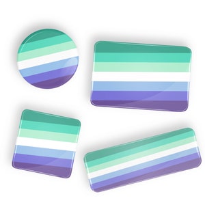 Puede incluir: Cuatro botones de diferentes tamaños con los colores de la bandera del orgullo genderqueer. La bandera tiene cinco franjas: verde claro, blanco, azul claro, azul oscuro y morado.